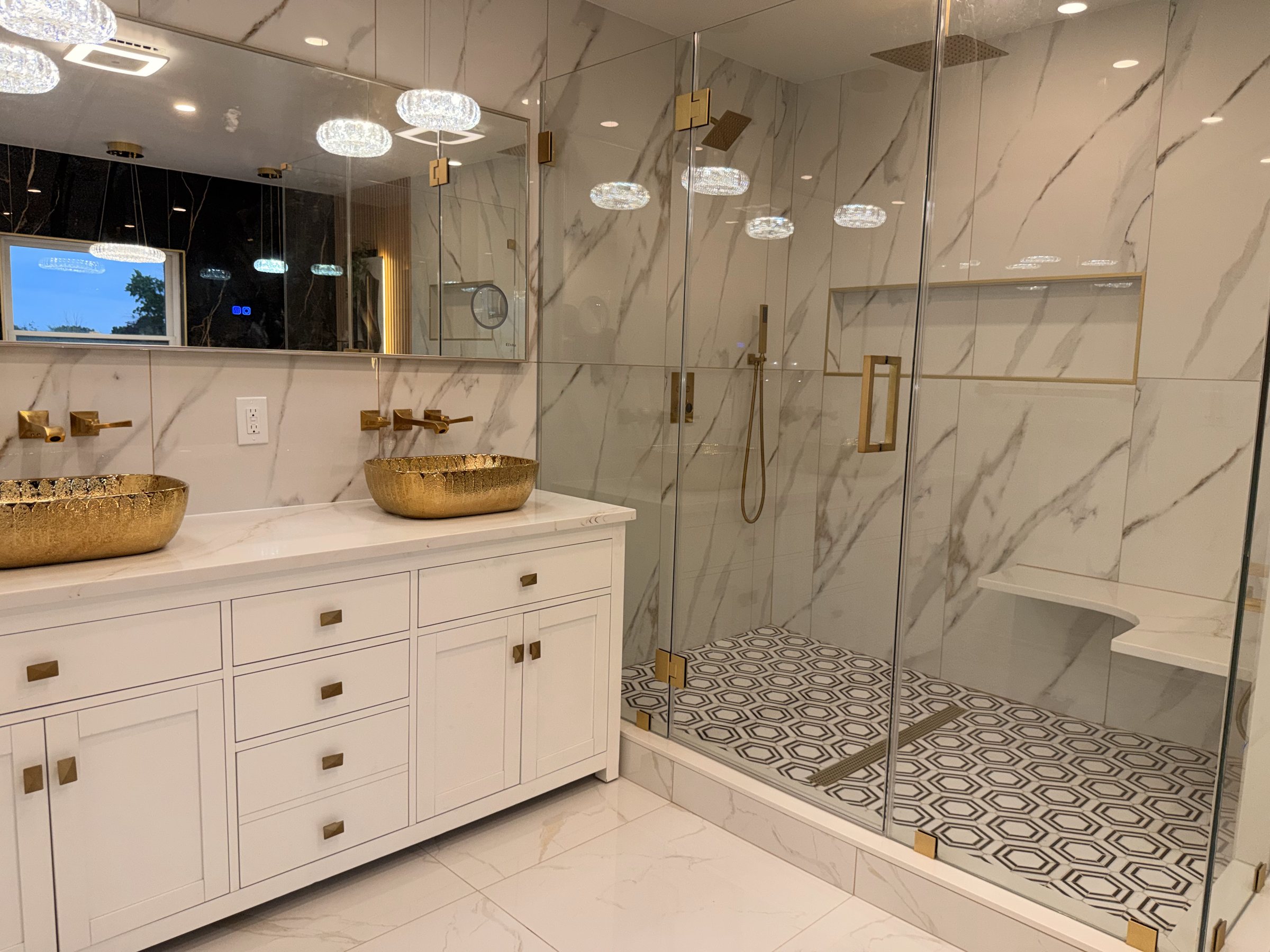 Marble bathroom with brass fixtures, gold vessel basins and a glass walk-in shower