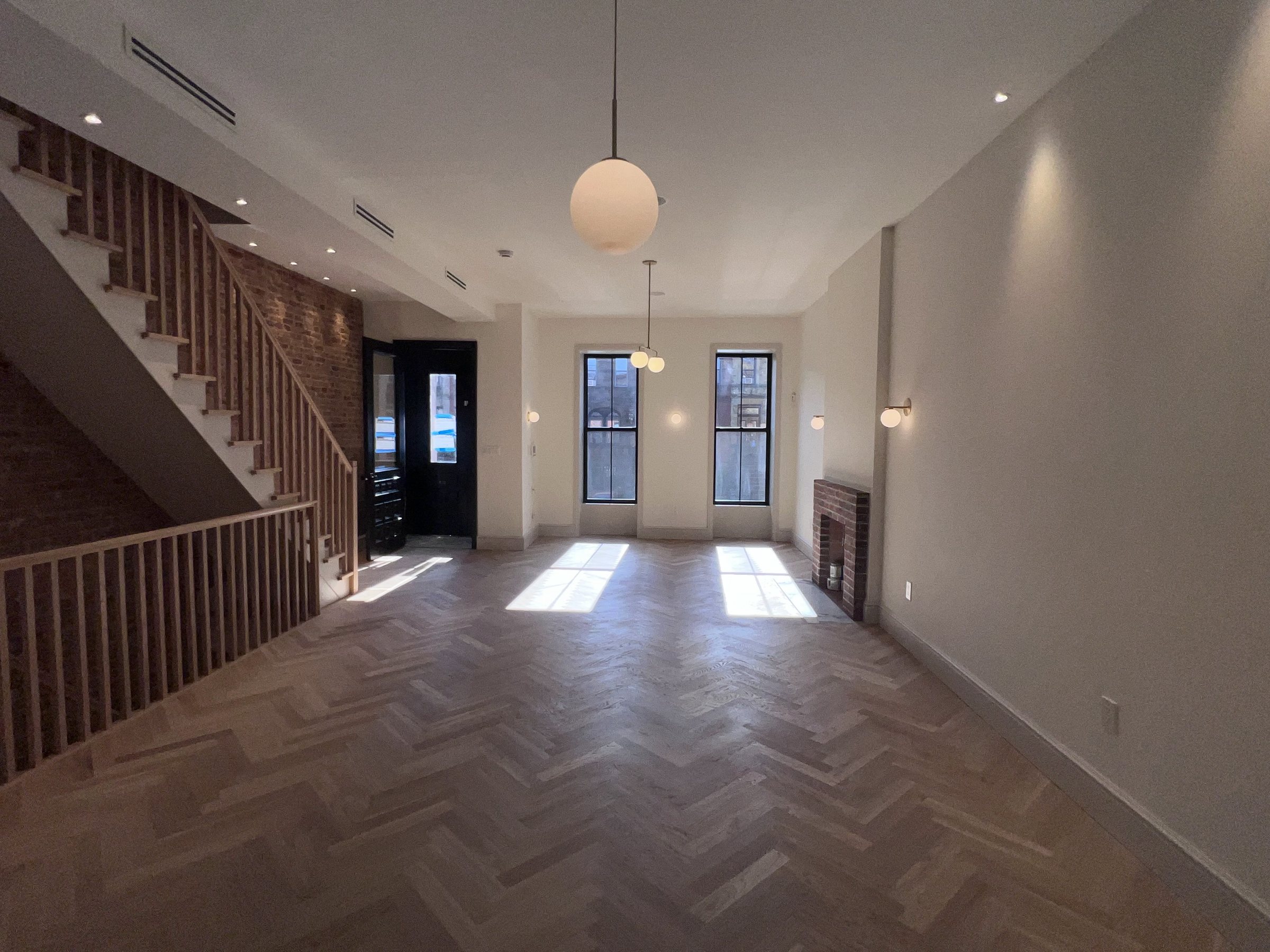Renovated brownstone parlour floor with herringbone oak flooring, exposed brick wall, restored staircase and original brick fireplace