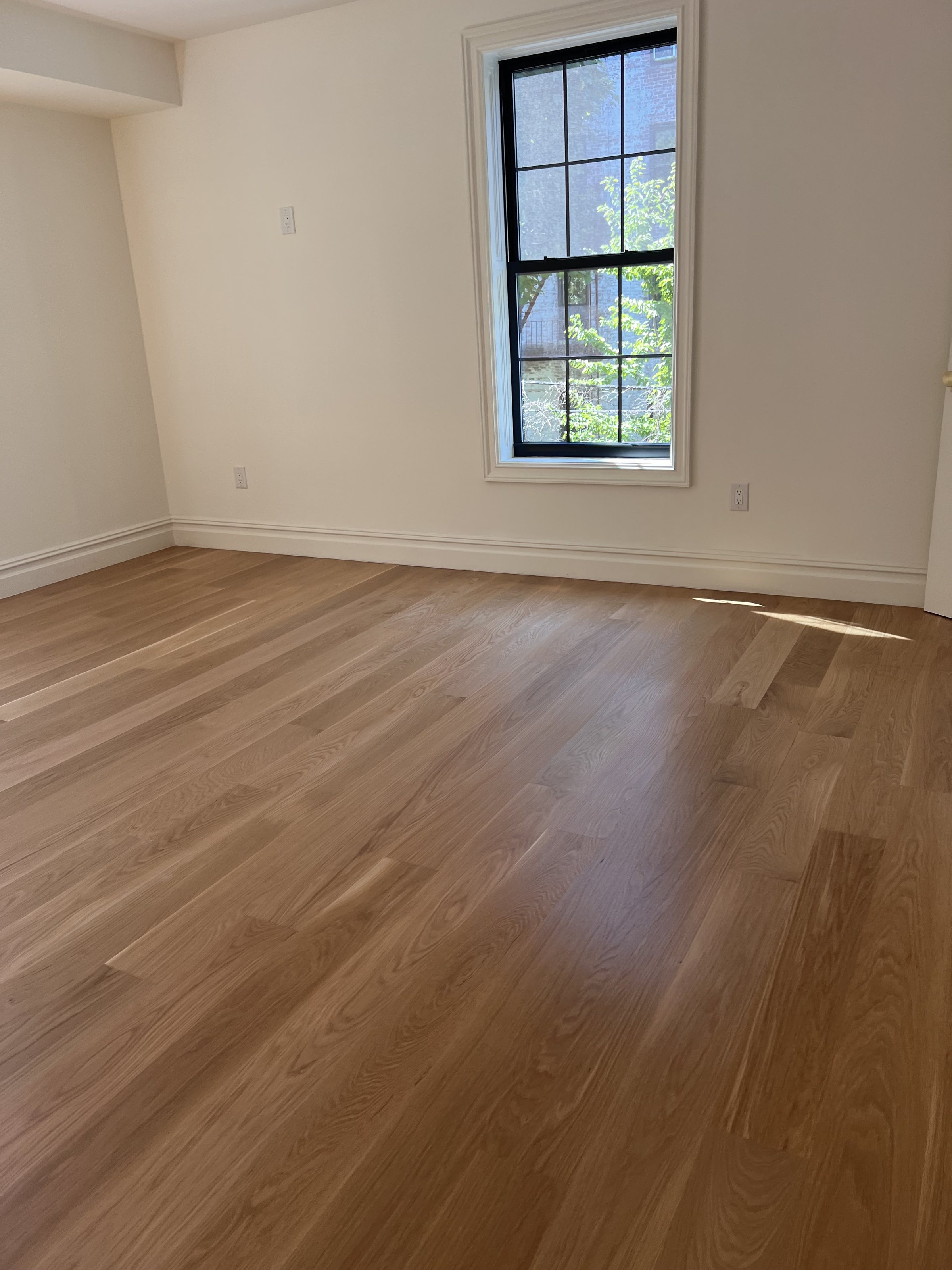 Finished room with wide oak plank flooring and a black steel-framed window