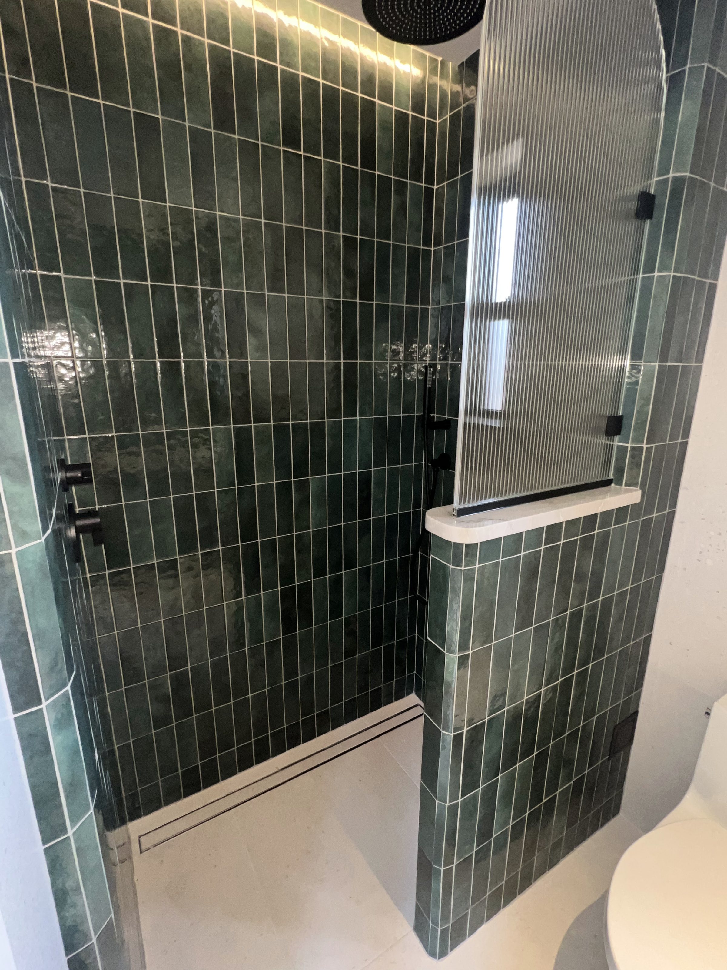 Walk-in shower tiled in stacked deep-green ceramic with fluted glass and black fixtures